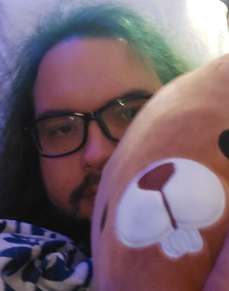 A man with green hair is lying with a beaver Squishmallow